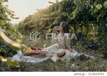 Woman picnic vineyard. Happy woman with a glass of wine at a picnic in the vineyard, wine tasting at sunset and open nature in the summer. Romantic dinner, fruit and wine. Woman picnic vineyard. Happy woman with a glass of wine at a picnic in the vineyard, wine tasting at sunset and open nature in the summer. Romantic dinner, fruit and wine. 112624452