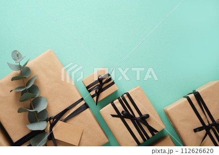 Brown craft gift boxes with black ribbons and Eucalyptus on mint background. Space for your text. Brown craft gift boxes with black ribbons and Eucalyptus on mint background. Space for your text. 112626620