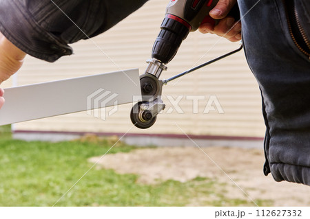 Gears for cutting sheet metal are rotated using an electric drill, being an adapter attachment, roofer cuts roofing steel outdoors. Gears for cutting sheet metal are rotated using an electric drill, being an adapter attachment, roofer cuts roofing steel outdoors. 112627332