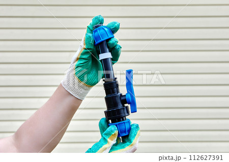 Installation of pipeline joint with ball valve using compression clamps, gloved hands on striped background of house wall. 112627391