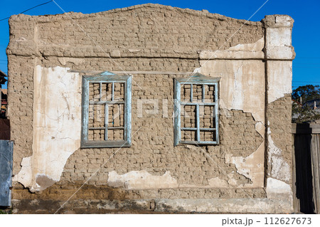 old house adobe air brick wall with two embedded wooden window frames and peeled off plaster leftovers - flat texture 112627673