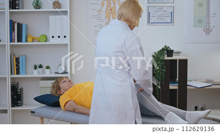 A certified orthopedist examines the knee of her patient, making a diagnosis in physiatry 112629136