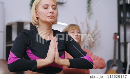 Two women practice deep breathing and relaxation, meditating together at home, embracing calmness and mindfulness 112629187