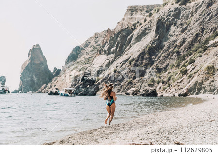 Woman beach vacation photo. A happy tourist in a blue bikini enjoying the scenic view of the sea and volcanic mountains while taking pictures to capture the memories of her travel adventure. 112629805