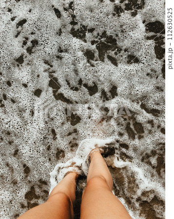 Woman legs barefoot at sea foam waves on sand beach summer day. top view above women feet. 112630525