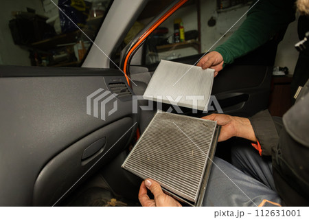Replacing the air filter in the car interior A man holds in his hands an old and a new air filter from the inside of a car. The man shows how dirty the old filter is and how much dust there is in it. 112631001
