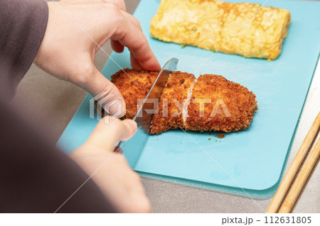 お弁当のトンカツを切る女性の手元 112631805