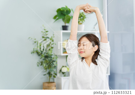 部屋で伸びをする女性 112633321