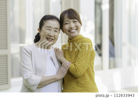 庭で笑顔で並んで立つシニア女性とミドルエイジの親子のポートレート 112633943