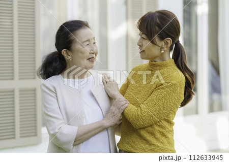 庭で笑顔で会話するシニア女性とミドルエイジの親子 庭で笑顔で会話するシニア女性とミドルエイジの親子 112633945
