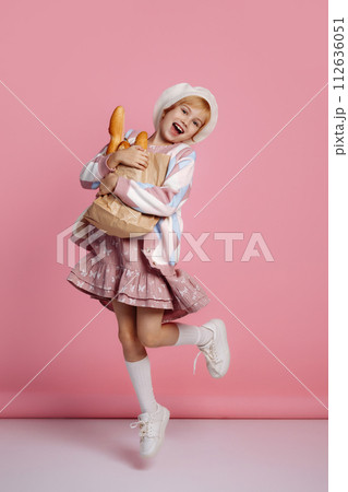 Joyful girl jumping with a bag of bread on a pink background 112636051