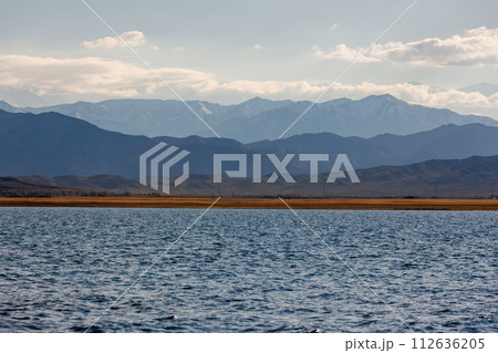 Blue calm water in Issyk-Kul lake with mountains on background at autumn afternoon 112636205