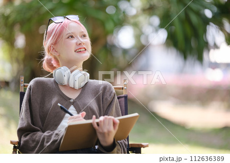Young Happy Artist woman drawing book and wearing headphones in the garden. 112636389