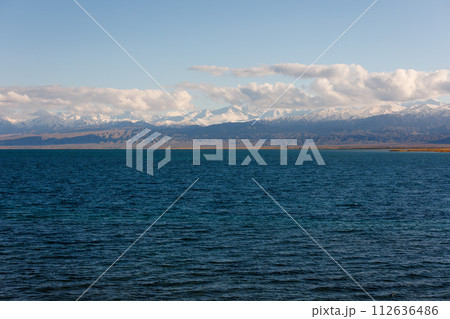 Blue calm water in Issyk-Kul lake with mountains on background at autumn afternoon 112636486