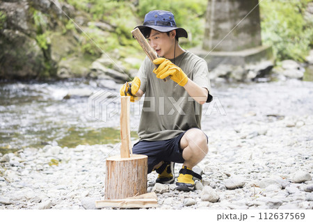 河原で薪割りをする若い男性 バトニングイメージ 河原で薪割りをする若い男性 バトニングイメージ 112637569