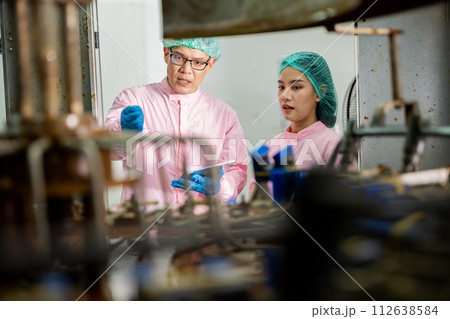 At the drinks production plant two factory machine engineers discuss quality control with a digital tablet. They concentrate on examining manufacturing processes in the beverages factory. At the drinks production plant two factory machine engineers discuss quality control with a digital tablet. They concentrate on examining manufacturing processes in the beverages factory. 112638584
