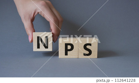 NPS - Net Promoter Score symbol. Wooden cubes with words NPS. Businessman hand. Beautiful grey background. Business and NPS concept. Copy space. 112641228