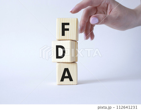 FDA - Food Drug Administration symbol. Wooden cubes with word FDA. Doctor hand. Beautiful white background. Medical and Food Drug Administration concept. Copy space. 112641231