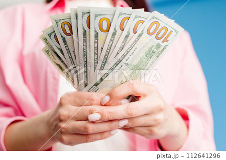Close-up of female hands counting stack of hundred dollar bills blue background 112641296