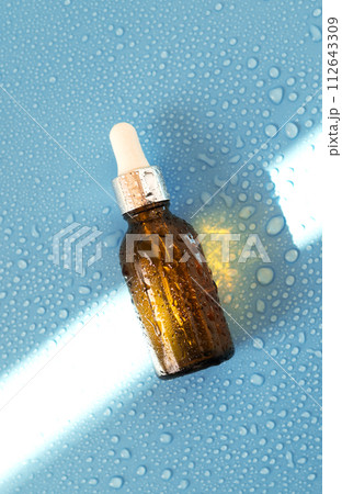 Serum bottle , oil cosmetic on blue background with hard light and water drops. with shadows flat lay, top view 112643309