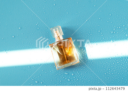 Perfume woman bottle on blue background with hard light and water drops. with shadows flat lay, top view 112643479