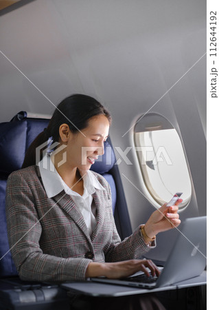Asian female using laptop computer and holding credit card in airplane, Business traveling and technology concept. Asian female using laptop computer and holding credit card in airplane, Business traveling and technology concept. 112644192