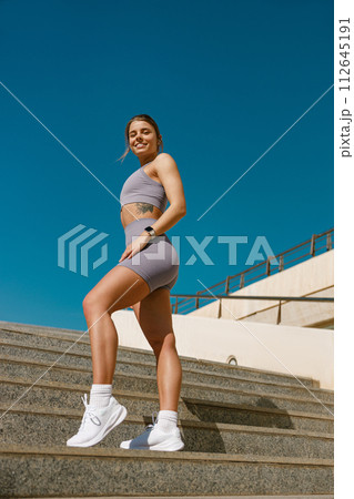 Young female athlete in sportswear have a rest after morning jogging outside and looks camera Young female athlete in sportswear have a rest after morning jogging outside and looks camera 112645191