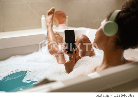 a woman is taking a bath in a bathtub while listening to music on her phone 112646368