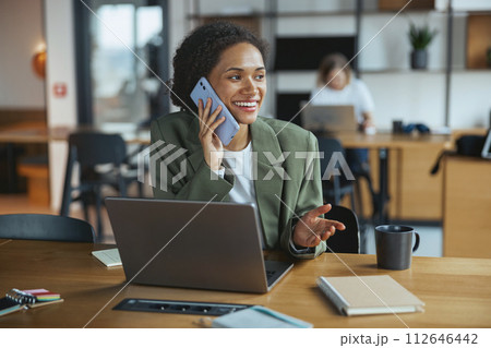 A whitecollar worker sits at a desk with a laptop and talks on a cell phone in nice modern coworking office A whitecollar worker sits at a desk with a laptop and talks on a cell phone in nice modern coworking office 112646442