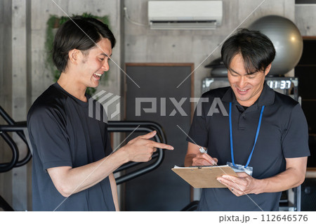 パーソナルトレーニングでカウンセリングを受ける若いアジア人男性とパーソナルトレーナーの男性 パーソナルトレーニングでカウンセリングを受ける若いアジア人男性とパーソナルトレーナーの男性 112646576