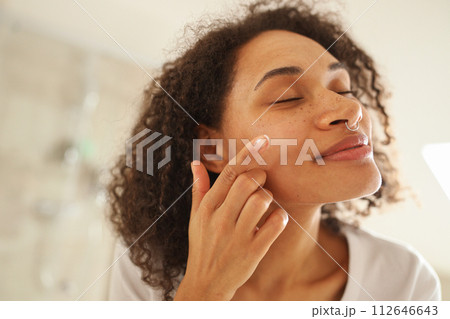 Woman applying lotion to her Forehead, Cheek, and Neck in front of mirror 112646643