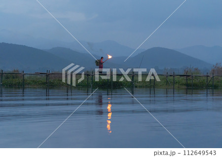 Burmese fisherman walking on bridge in Unle lake, natural river in Asia in Myanmar. People lifestyle. 112649543