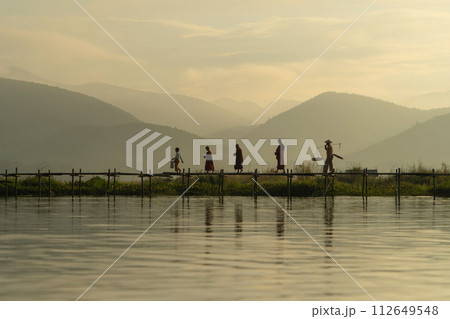 Burmese fisherman walking on bridge in Unle lake, natural river in Asia in Myanmar. People lifestyle. 112649548