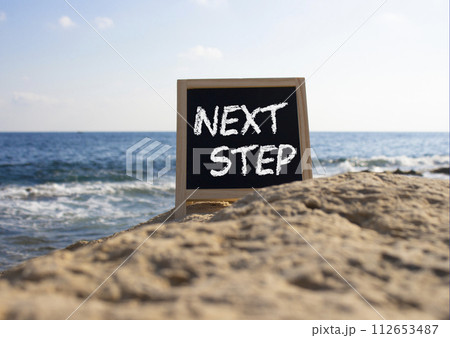 Next Step symbol. Concept words Next Step on black chalk background. Beautiful sea background. Business and Next Step concept. Copy space. Next Step symbol. Concept words Next Step on black chalk background. Beautiful sea background. Business and Next Step concept. Copy space. 112653487