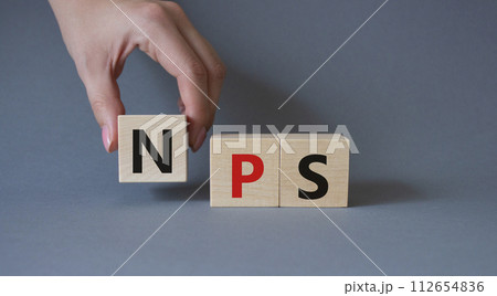 NPS - Net Promoter Score symbol. Wooden cubes with words NPS. Businessman hand. Beautiful grey background. Business and NPS concept. Copy space. 112654836