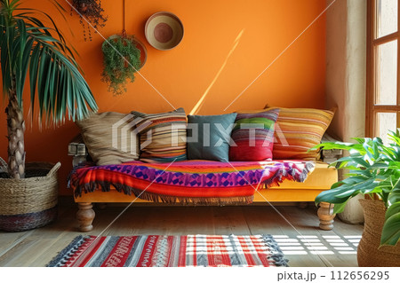Beige sofa with multicolored cushions, blanket and large floor plant near window in mexican style next to empty yellow wall mock up with copy space Beige sofa with multicolored cushions, blanket and large floor plant near window in mexican style next to empty yellow wall mock up with copy space 112656295