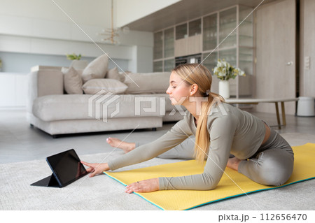 Young woman practices yoga at home, with tablet pc next to her, classes at home Young woman practices yoga at home, with tablet pc next to her, classes at home 112656470