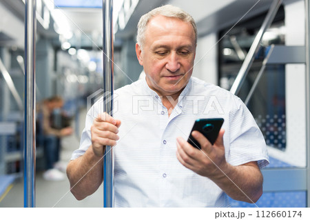 Mature man with smartphone standing in subway car 112660174