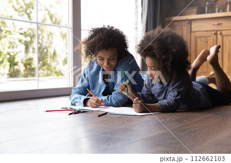 African mom and daughter lying on floor draw in sketchbook 112662103