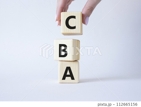 CBA - Cost Benefit Analysis symbol. Wooden cubes with word CBA. Beautiful white background. Businessman hand. Business and Cost Benefit Analysis concept. Copy space. CBA - Cost Benefit Analysis symbol. Wooden cubes with word CBA. Beautiful white background. Businessman hand. Business and Cost Benefit Analysis concept. Copy space. 112665156