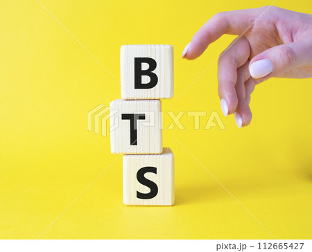 BTS symbol. Wooden cubes with word BTS. Businessman hand Beautiful yellow background. BTS concept. Copy space. BTS symbol. Wooden cubes with word BTS. Businessman hand Beautiful yellow background. BTS concept. Copy space. 112665427
