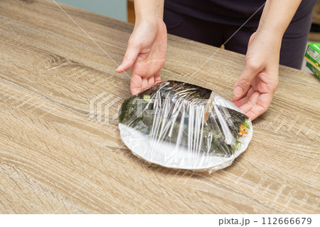 巻き寿司にラップを巻く女性の手元 112666679