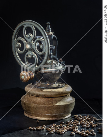 Antique coffee original grinder metal shake wheel with hand crank and coffee beans on dark background. 112667436