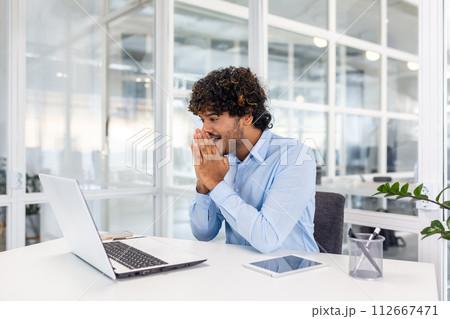 Happy joyful hispanic businessman inside office reading online happy news on laptop, young entrepreneur celebrating successful achievement results. 112667471