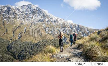 Hikers walking towards snowy mountain during sunny autumn day, New Zealand 112670817