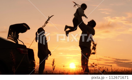 Silhouette of father tossing child in air. Family traveling by car having fun in nature laughing smiling enjoying life. Happy moments together. Loving dad with daughter and wife at weekend travel trip 112671671