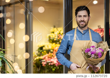 Cheerful male florist holding a beautiful bouquet, ready to greet customers at the entrance of his well-lit flower shop. Cheerful male florist holding a beautiful bouquet, ready to greet customers at the entrance of his well-lit flower shop. 112673720