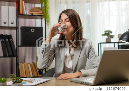 Focused businesswoman girl sitting at workplace desk drinking water while working with office laptop 112674093
