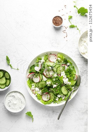 Radish and cucumber fresh green leafy vegetable salad with romaine lettuce, cottage cheese and yogurt, top view Radish and cucumber fresh green leafy vegetable salad with romaine lettuce, cottage cheese and yogurt, top view 112675454