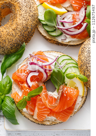Salmon sandwiches with bagel, salted fish, fresh cucmber, onion and basil on white background, top view. Healthy breakfast with salmon toasts Salmon sandwiches with bagel, salted fish, fresh cucmber, onion and basil on white background, top view. Healthy breakfast with salmon toasts 112675497